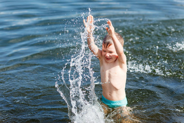 Joyful boy swimming in the lake and splashing in the water. Boy play in water in summer. 