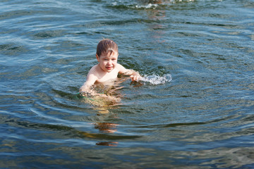 Joyful boy swimming in the lake and splashing in the water. Boy play in water in summer. 