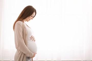 Beautiful pregnant woman hugging her tummy at home - Powered by Adobe