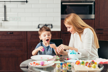 Funny little boy opens his mouth to eat homemade Easter egg, that they painted out together with his Mum, hapy and hungry after creative activities