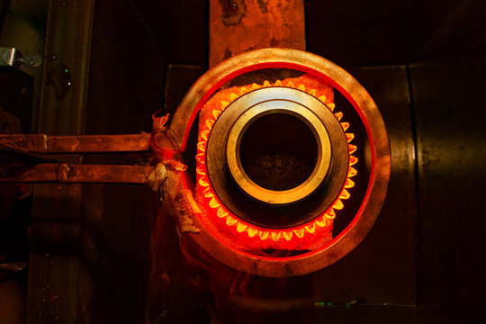 closeup calcining hot metal steel gear parts in a factory induction furnace with smoke