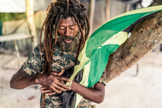 African American bearded male with dreadlocks holding Jamaica flag near tree