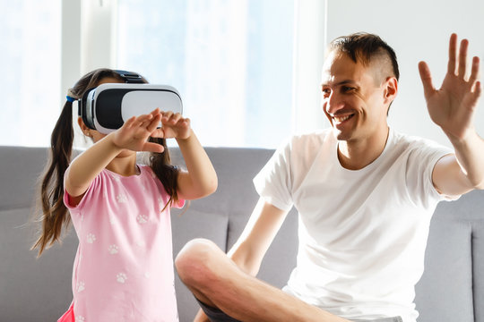 family, virtual reality and entertainment concept - happy father and little daughter with vr glasses playing video game at home in evening