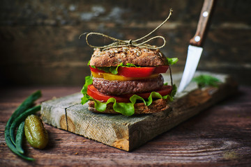 Tasty fresh burger tied with linen thread lying on shabby lumber board