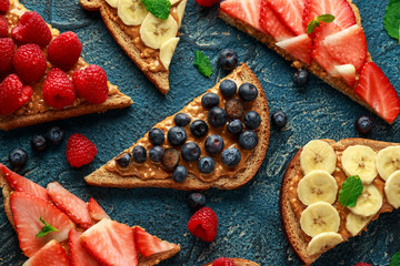Peanut butter sandwiches with fresh strawberry, blueberry, raspberry and banana whole meal toasts.