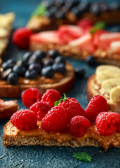 Peanut butter sandwiches with fresh strawberry, blueberry, raspberry and banana whole meal toasts.