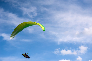 Yellow and green paraglider is flying in the blue sky against the background of clouds. Paragliding...