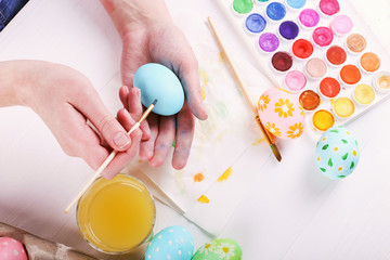 Hand painted Easter eggs, paints and brushes on a white table. Preparation for the holiday. Girls hands draw a pattern.