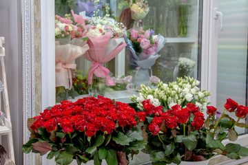 fresh flowers - red roses and white eustomas - in front of a floristry shop window, where elegant delicate bouquets stand in anticipation of a buyer