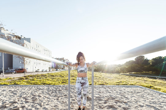 Attractive slim lady in sportswear doing exercises on parallel bars on court near buildings