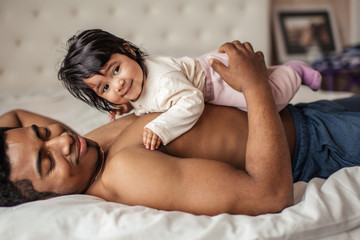 smiling little baby having a rest on her father's stomack, close up side view photo. preparation for sleeping