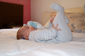 cute 4 months old baby boy lying on bed and playing with his legs