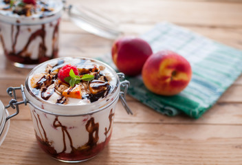 Close-up of peach parfait with yogurt, granola and chocolate topping in a jar