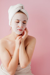 Beautiful young woman is applying a cosmetic tissue mask on a face on a pink background