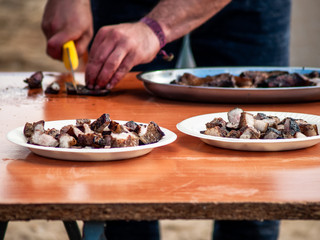 Unrecognizable person cutting meat with a knife and placing it on a paper plate in the street at a popular party in a village in Spain