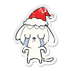 cute distressed sticker cartoon of a dog crying wearing santa hat