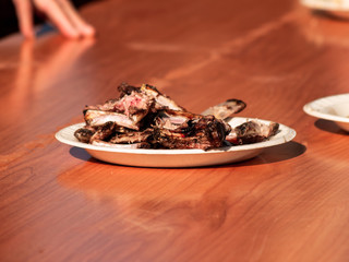 Unrecognizable person taking meat cooked from a paper plate in the street at a popular party in a village in Spain