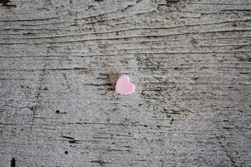 One tiny pink sugar candy heart sprinkle lying on wooden table symbolizing loneliness, lost love,...