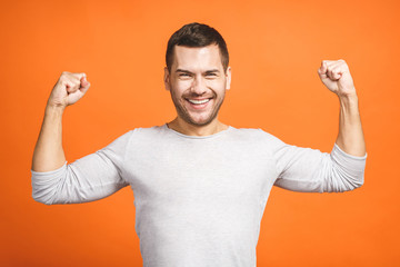 Happy winner. Happy young handsome man gesturing and keeping mouth open while standing against orange background.