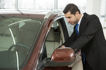 Handsome young businessman choosing a new car at the dealership salon