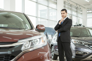 Handsome young businessman choosing a new car at the dealership salon