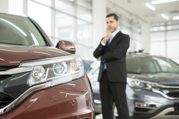 Handsome young businessman choosing a new car at the dealership salon