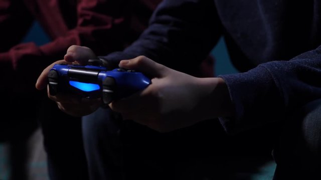 Close up teenager gamer's hands using joystick for playing with best friend video game on home console at late evening. Sitting on sofa teen boy actively pressing buttons of remote game controller