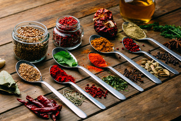 Bunch of assorted spices placed in order on lumber tabletop near bottle of oil