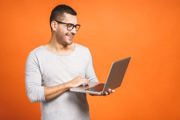 Confident business expert. Confident young handsome man in casual holding laptop and smiling while standing against orange background.