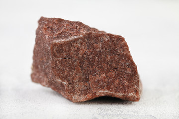 Natural mineral from geological collection - raw pink quartzite stone from Shoksha, Karelia, Russia on white cement background.
