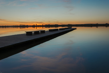 A long bridge with benches, a sunset and a calm lake