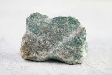 Natural rock specimens - green listvenite, listwanite mineral from Berezovsk, Ural, Russia on white cement background.