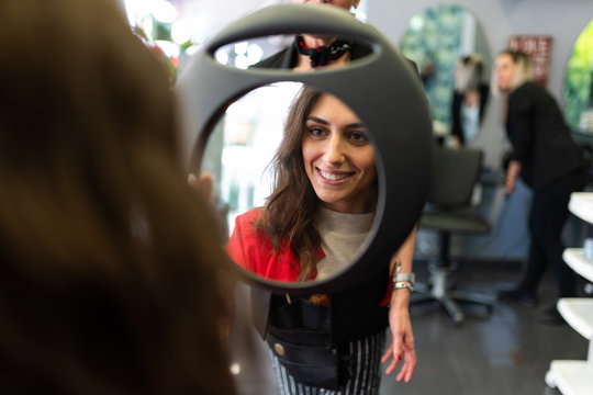 Stylist Holding Mirror With Reflection Of Attractive Cheerful Lady In Hairdressing Salon