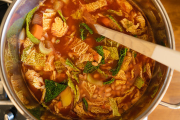 Pot with homemade Minestrone soup, a traditional Italian one pot dish made of tomatoes, carrots, onions, savoy cabbage, cannellini beans, celery and potatoes for a healthy vegetarian low carb diet