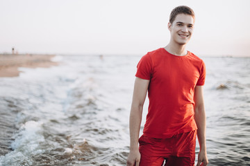 Fototapeta na wymiar Outdoor portrait of young european happy positive sportsman walking on the coast of sea. Freedom, emotional, sport concept