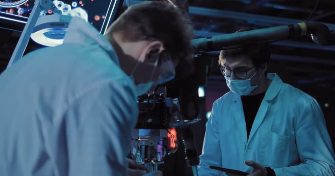 Young surgeons working on an experiment in the laboratory. Devices are connected, scientists are wearing white robe and glasses.