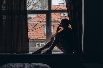Silhouette ot young sexy sad woman sitting near window and smoking