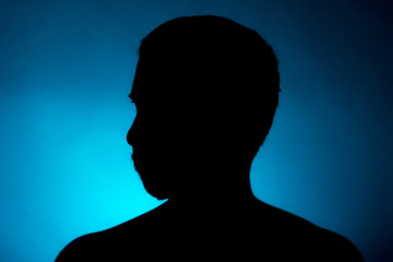 Cleanly defined silhouette of a male person turned to the left against a blue background with a spotlight and bright area right behind the bust. Studio shot with strong explicit colour background.