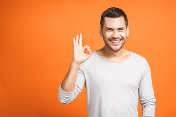 Portrait of a cheerful young man showing okay gesture isolated on the orange background. Ok sign.