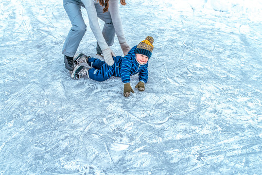 A small boy 2-5 years old, fell on the ice in the winter ice skating. Mom raises her son. Happy smiles. Learning skating support the first fall. Free space for text.