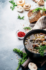 Hot thick mushroom soup with beef, spices and wholegrain barley, meat broth. With black bread, in metal pan, top view, flat lay, gray kitchen table backgound