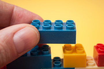 closeup of hand of man playing with colorful  plastic bricks construction on yellow background