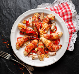 Spicy chicken meat, Grilled chicken tenderloin wrapped with bacon with addition chili peppers, garlic and herbs on white plate, black background