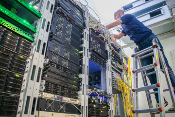 Engineer is laying and connecting the wires. A specialist stands on the ladder in the server room of the data center. Repair of telecommunication equipment.  Repair of telecommunication equipment