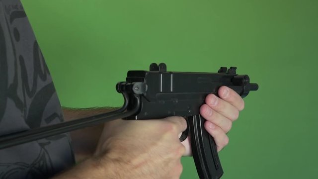 Medium shot of a man shooting a machine gun with shoulder stock unfolded towards green screen
