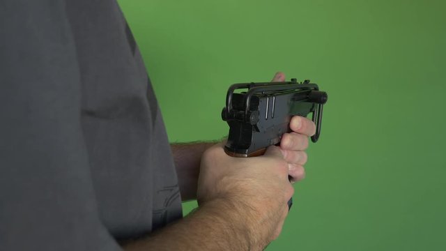 Medium shot of a man shooting a machine gun with shoulder stock folded towards green screen