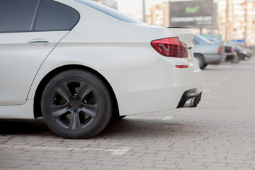 Side view of white car parked in paved parking lot area on blurred suburb road background on bright...