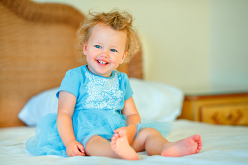 Fototapeta premium Lovely happy blonde toddler girl sitting on a bed