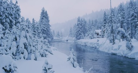 Beautiful snowy river forest scene with cabin and snowflakes falling, amazing winter nature scene