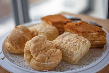 Different types of European pastries (napoleon, walnaut and eclair cakes) on white plate on blurred...